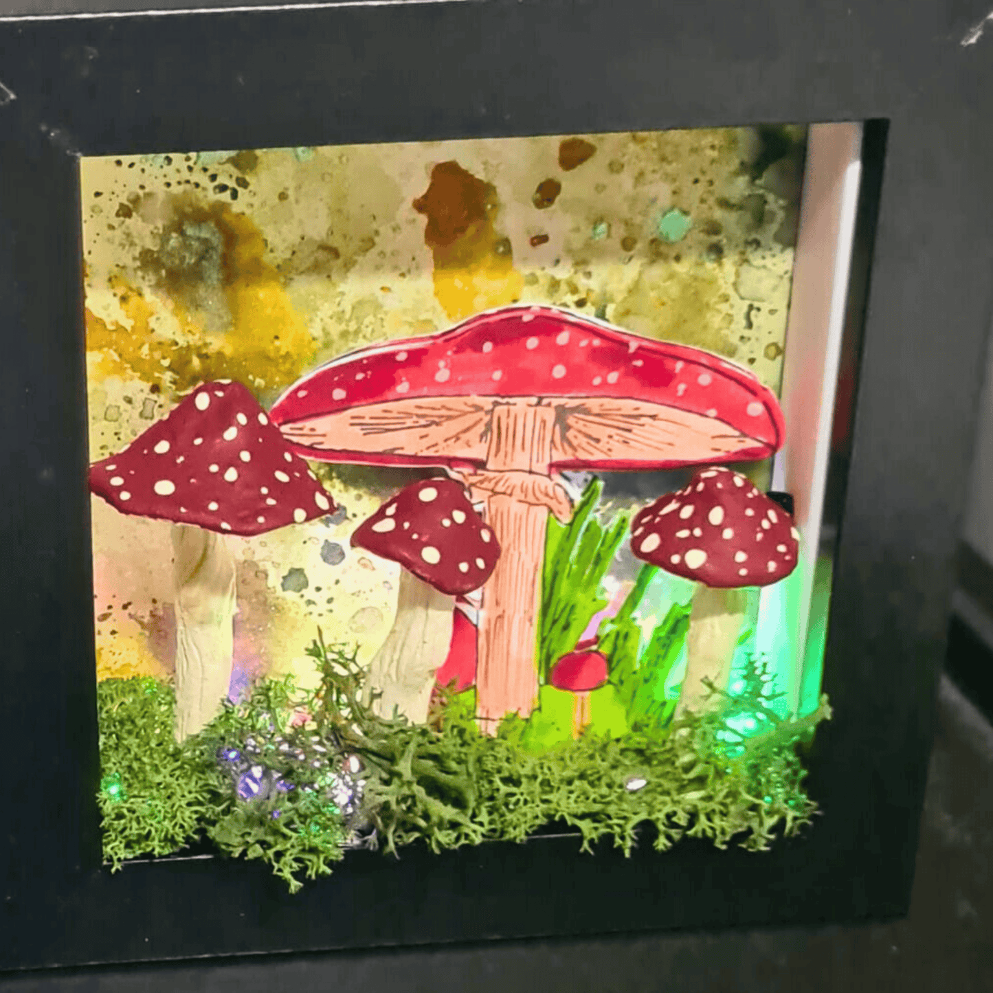 Completed 3D mixed media woodland scene from “Whisper of The Woodland” kit, featuring sculpted mushrooms, moss, fairy lights, and layered textures inside a shadow box frame.